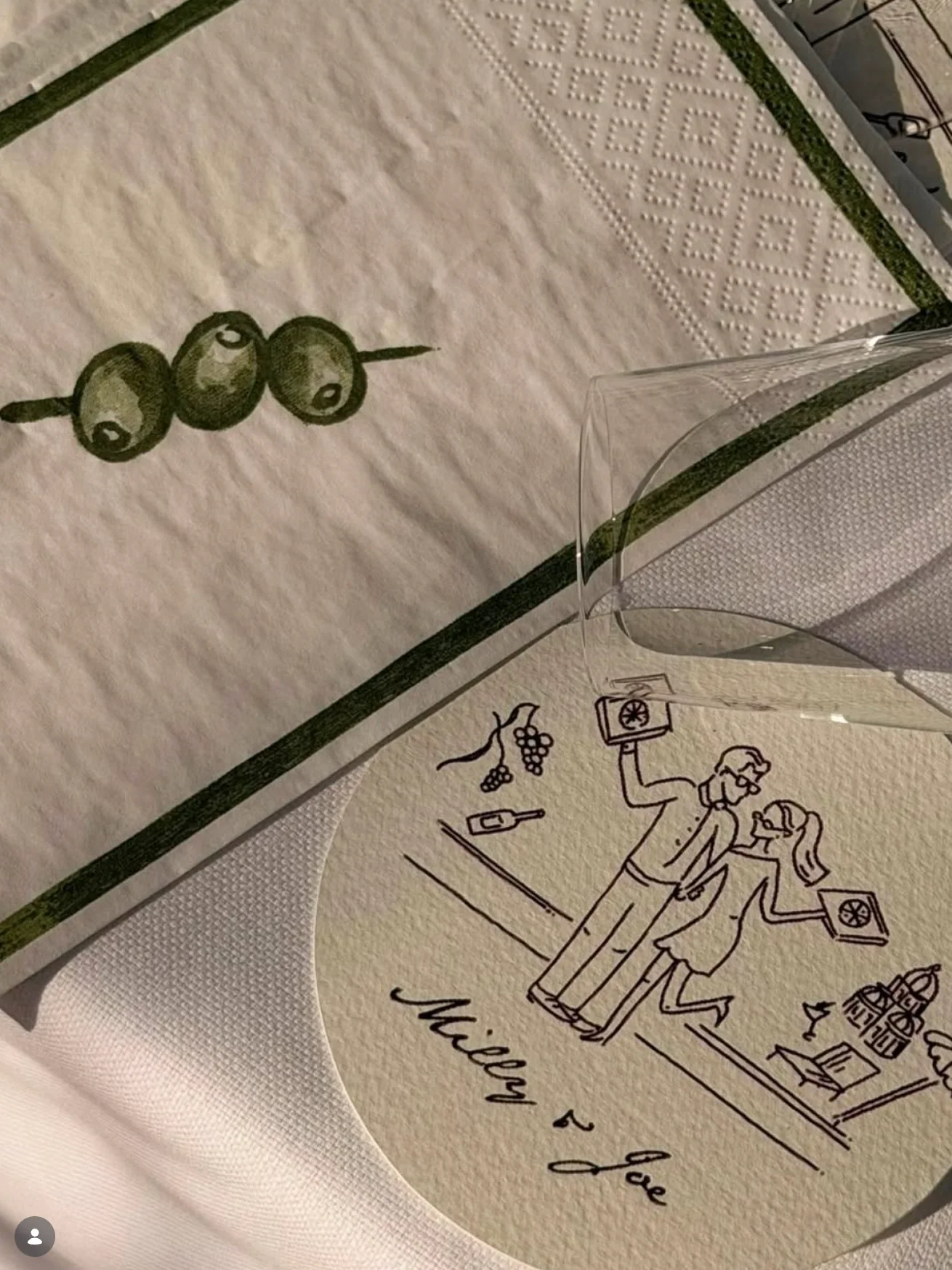 An illustrated coaster and olive napkin on a wedding table